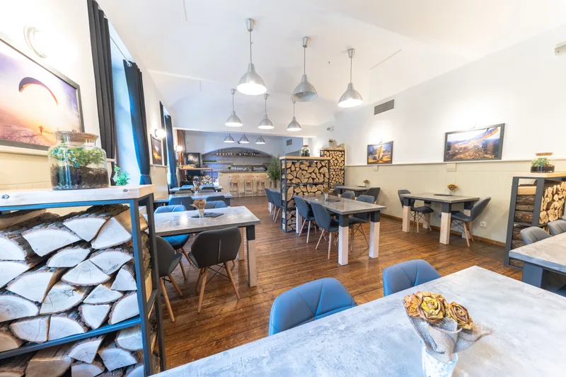 Útulný interiér restaurace Do Nebe Písek – betonové stoly, modré židle a paraglidingové fotografie
