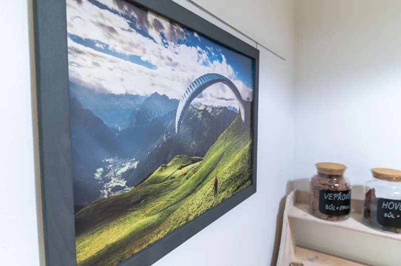 Zarámovaná fotografie paraglidistu nad horami na stěně restaurace Do Nebe Písek